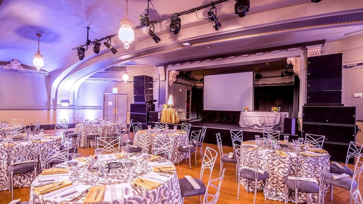 Round banquet tables set for a reception in a San Francisco event hall with a stage