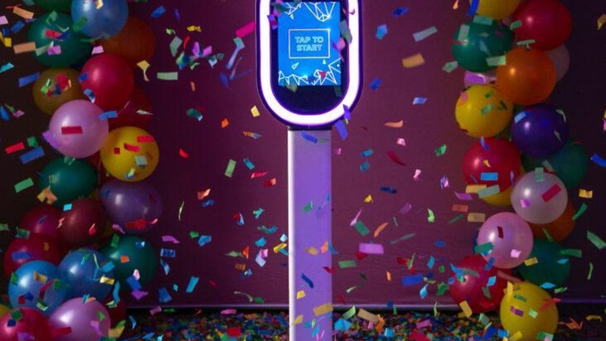 Ring-light photo booth kiosk set up between balloon garlands with confetti falling at an event